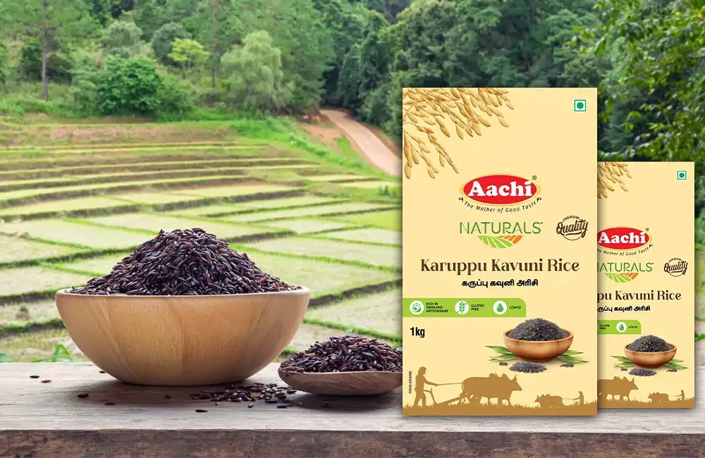 Aachi Karuppu Kavuni Rice packs placed beside wooden bowls filled with black rice, with paddy fields in the background.