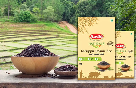Aachi Karuppu Kavuni Rice packs placed beside wooden bowls filled with black rice, with paddy fields in the background.
